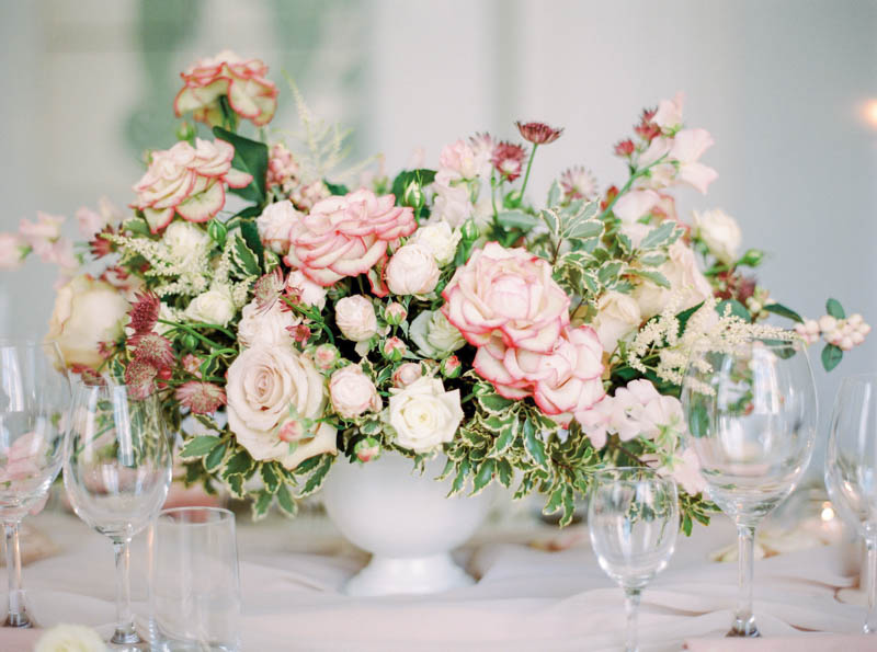 Garden inspired wedding floral arrangement with roses and summer flowers in light pink shades placed on a table with flowing fabric
